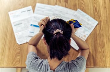 Top view of stressed young sitting Asian woman hands holding the head worry about find money to pay credit card debt and all loan bills. Financial problem concept.