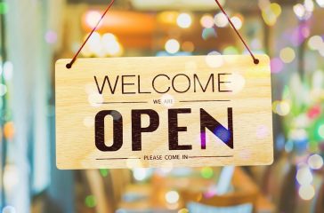 A business sign that says open on cafe or restaurant hang on door at entrance.