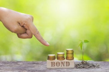 BOND WORD WITH BUSINESSMAN HAND POINTING TO STACK OF GOLD COIN.