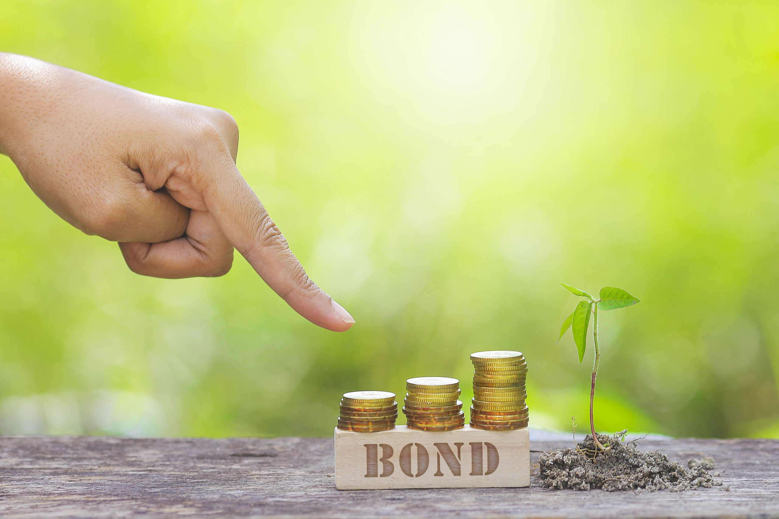 BOND WORD WITH BUSINESSMAN HAND POINTING TO STACK OF GOLD COIN.