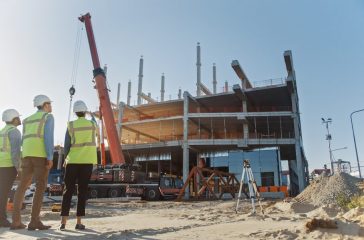 Diverse Team of Specialists Inspect Commercial, Industrial Building Construction Site. Real Estate Project with Civil Engineer, Investor and Worker. In the Background Crane, Skyscraper Formwork Frames