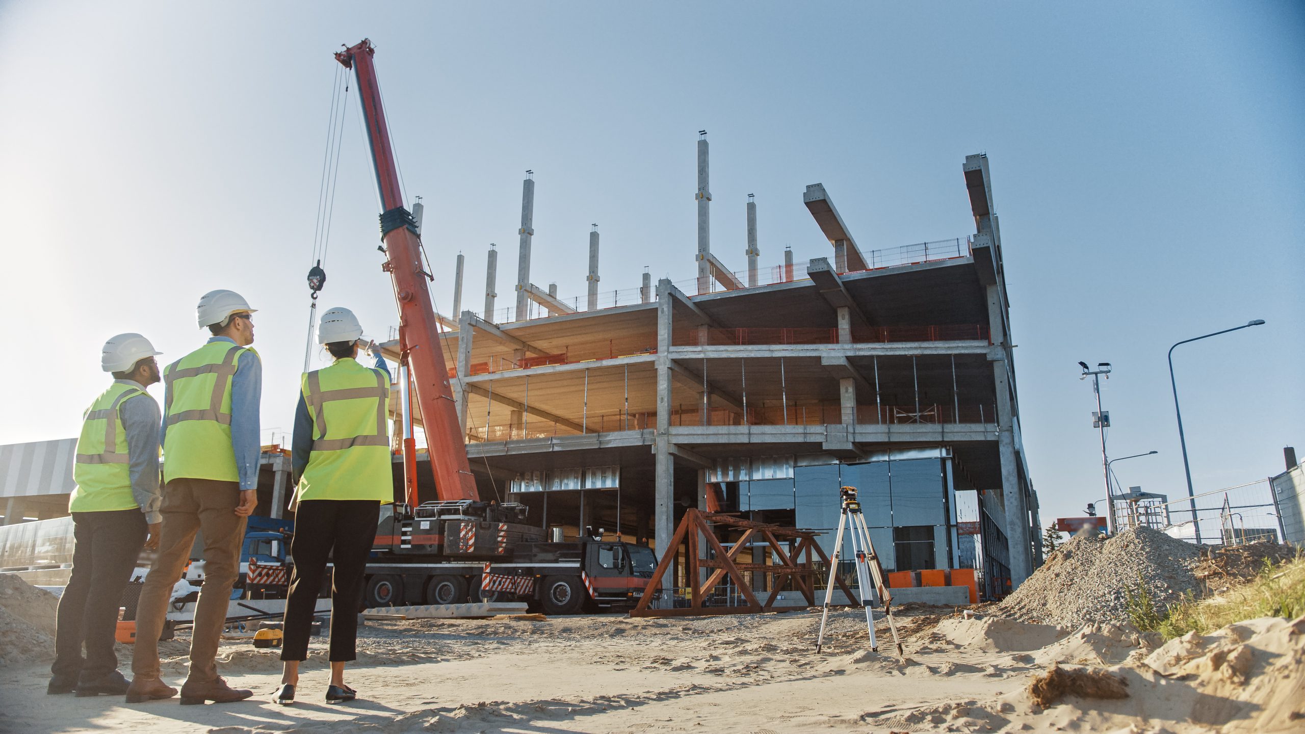 Diverse Team of Specialists Inspect Commercial, Industrial Building Construction Site. Real Estate Project with Civil Engineer, Investor and Worker. In the Background Crane, Skyscraper Formwork Frames