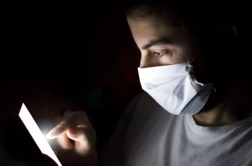 Close up of Young Man use Smart Phone at Night with Mask. Coronavirus.