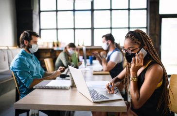 Portrait of young businesspeople with face masks working indoors in office.