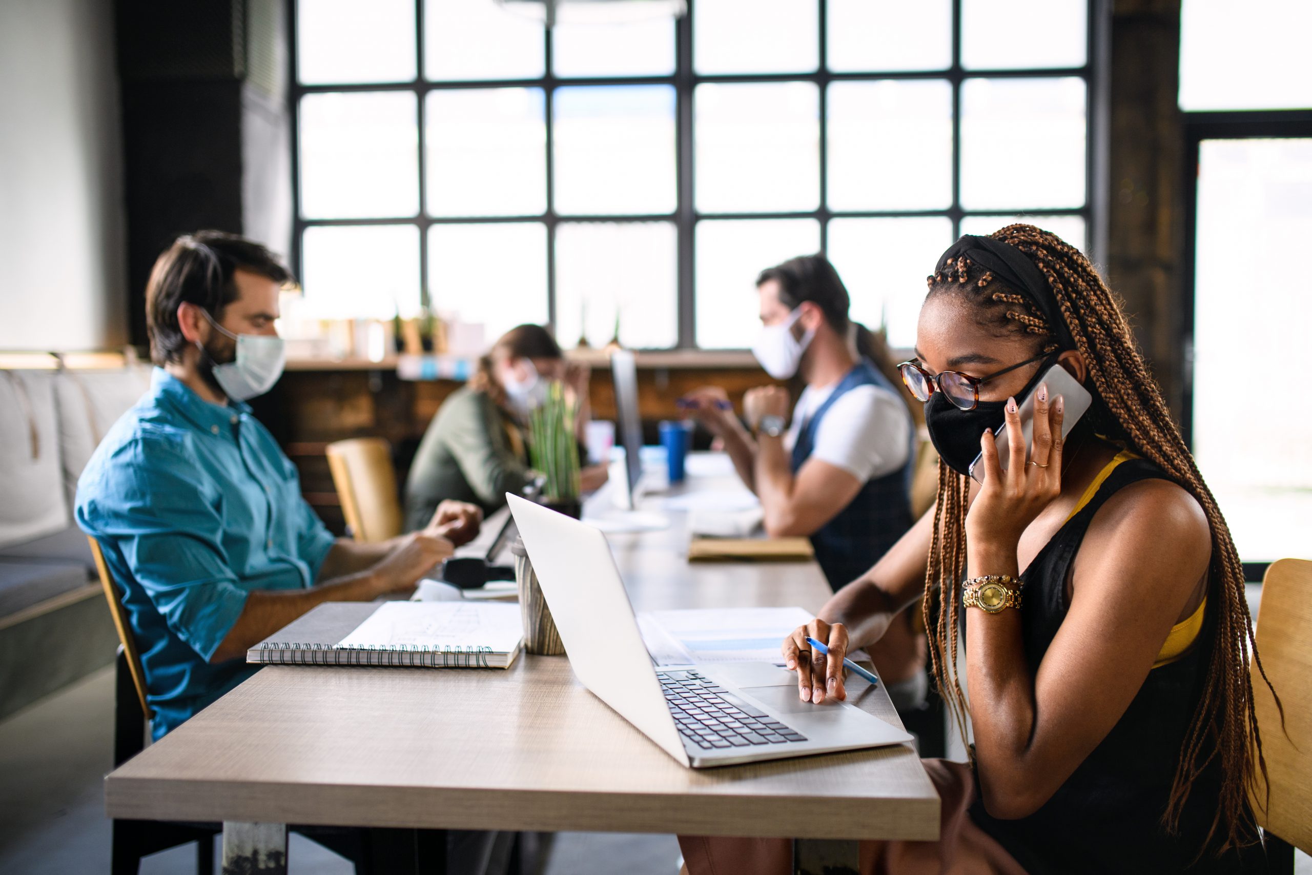 Portrait of young businesspeople with face masks working indoors in office.