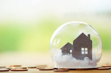 selective focus of miniature tiny home with stack coins on wooden floor over blurred green garden background,  Image for real-estate management  concept.