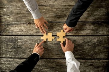 Four successful business men joining two puzzle pieces each bein