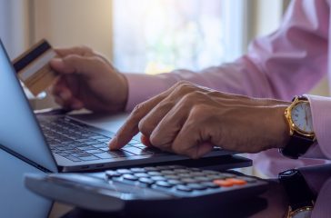 Business man makes online payment and internet banking by using laptop computer notebook and credit or debit card with calculator on the desk at home . Online banking, e business, e-commerce concept.