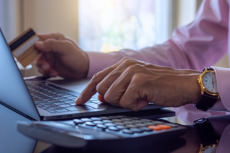 Business man makes online payment and internet banking by using laptop computer notebook and credit or debit card with calculator on the desk at home . Online banking, e business, e-commerce concept.