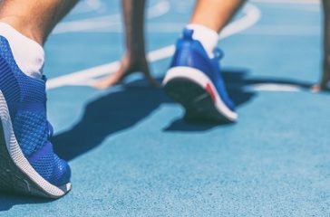 Sprinter waiting for start of race on running tracks at outdoor stadium. Sport and fitness runner man athlete on blue run track with running shoes. Banner panorama.