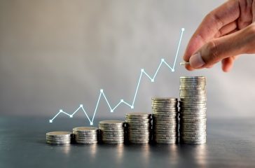 Hand stacking coins on black wooden table with profit line chart growth up. Business, finance, marketing, e-commerce concept and design