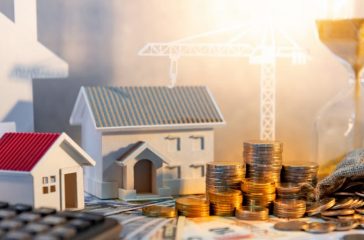 Real estate or property development. Construction business investment concept. Home mortgage loan rate. Coin stack on international banknotes with calculator, house and crane models on the table.