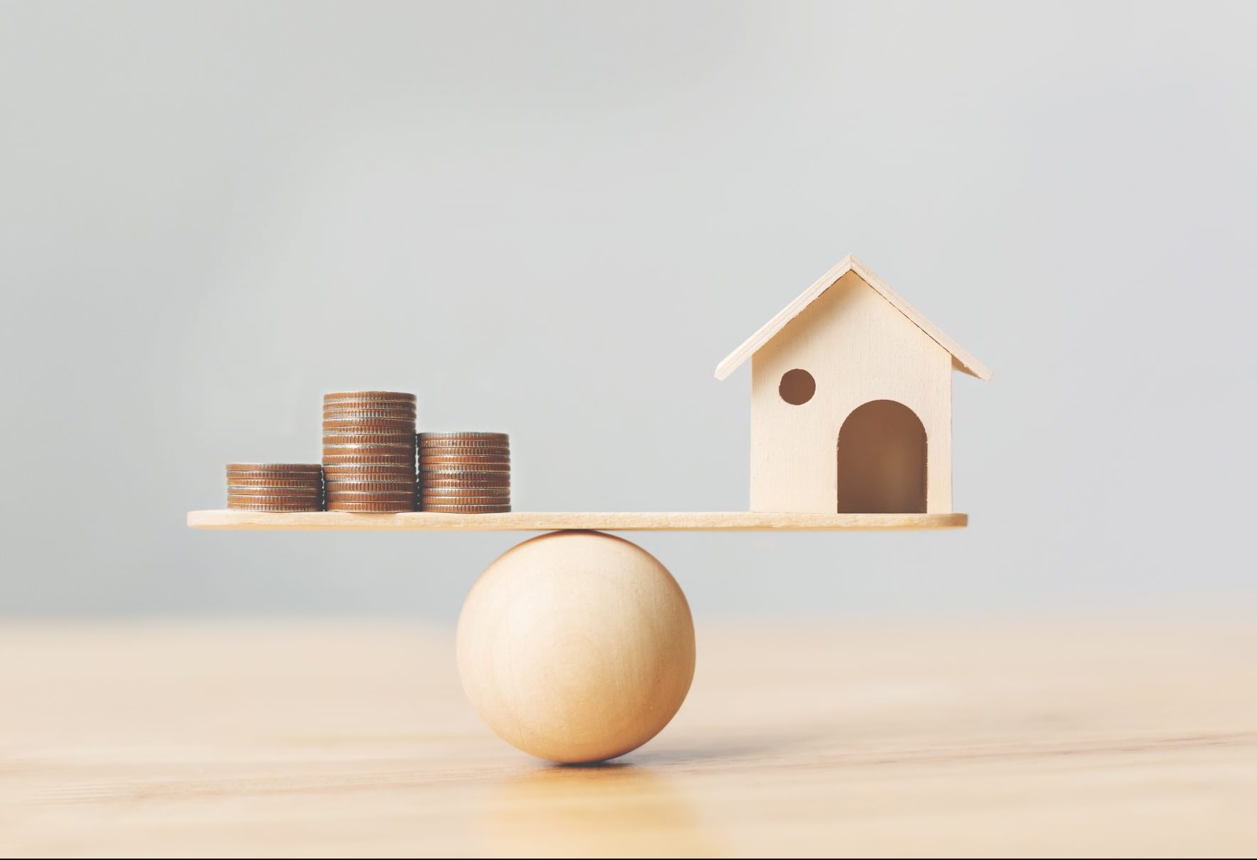 Wooden home and money coins stack on wood scale. Property investment and house mortgage financial real estate concept