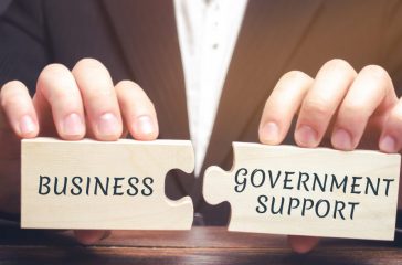 Businessman collects puzzles with the words Business and government support. Tax relief. Protection of manufacturers in the domestic market and promotion in foreign markets. Exemption from taxes.