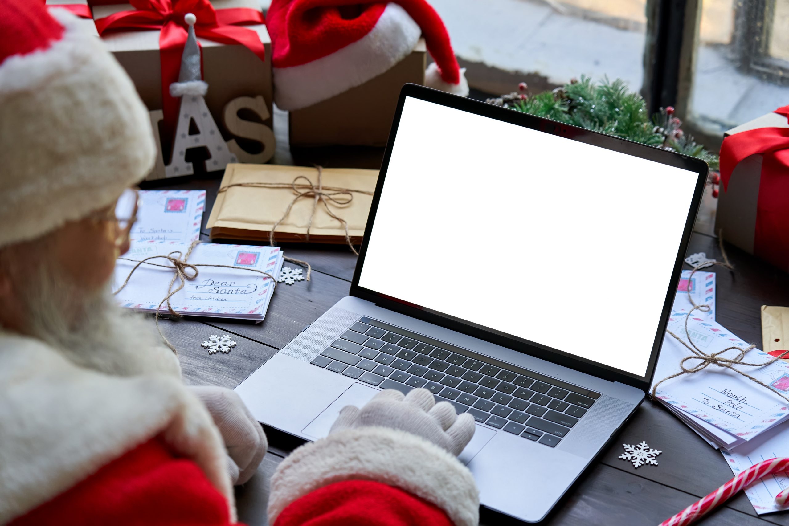 Santa Claus using laptop computer mock up white screen sitting at table.