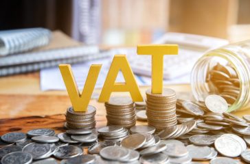Vat Concept.Word vat with stacked coins there is a notebook calculator on the desk.VAT