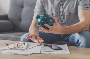 Man sitting at a table full of unpaid bills shakes out the last penny from the piggy bank. Spend your last savings. Unemployment, poverty, bankruptcy concept.