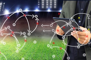 Football manager planning tactic with soccer field and bright spotlights.