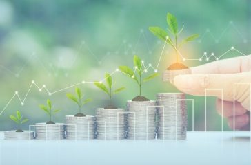 Finance,Woman hand holding plant growing on stack of coins money and graph on natural green background, investment and business concept