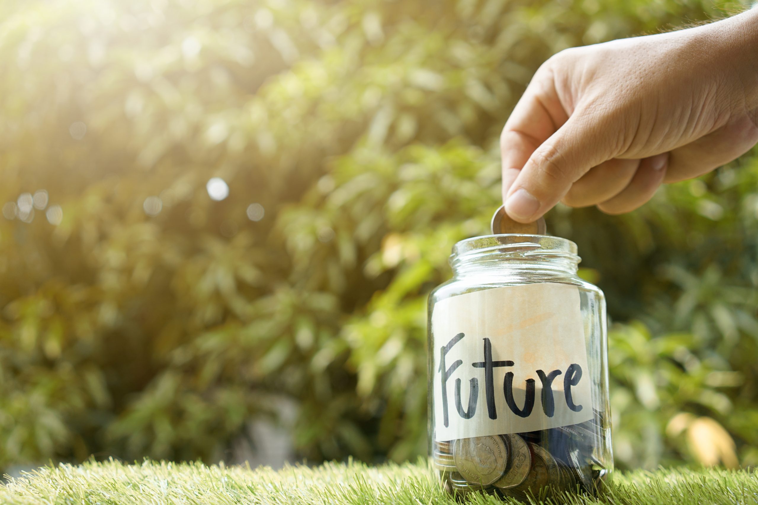 Money saving, Hand putting coin in glass jar with coins inside For now and future money. Concept of saving money for future.