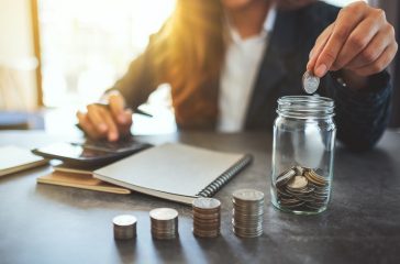 Closeup image of a businesswoman stacking and putting coins in a glass jar