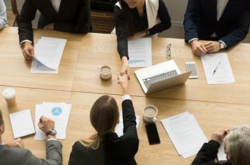 Two businesswomen shaking hands at group meeting, top view