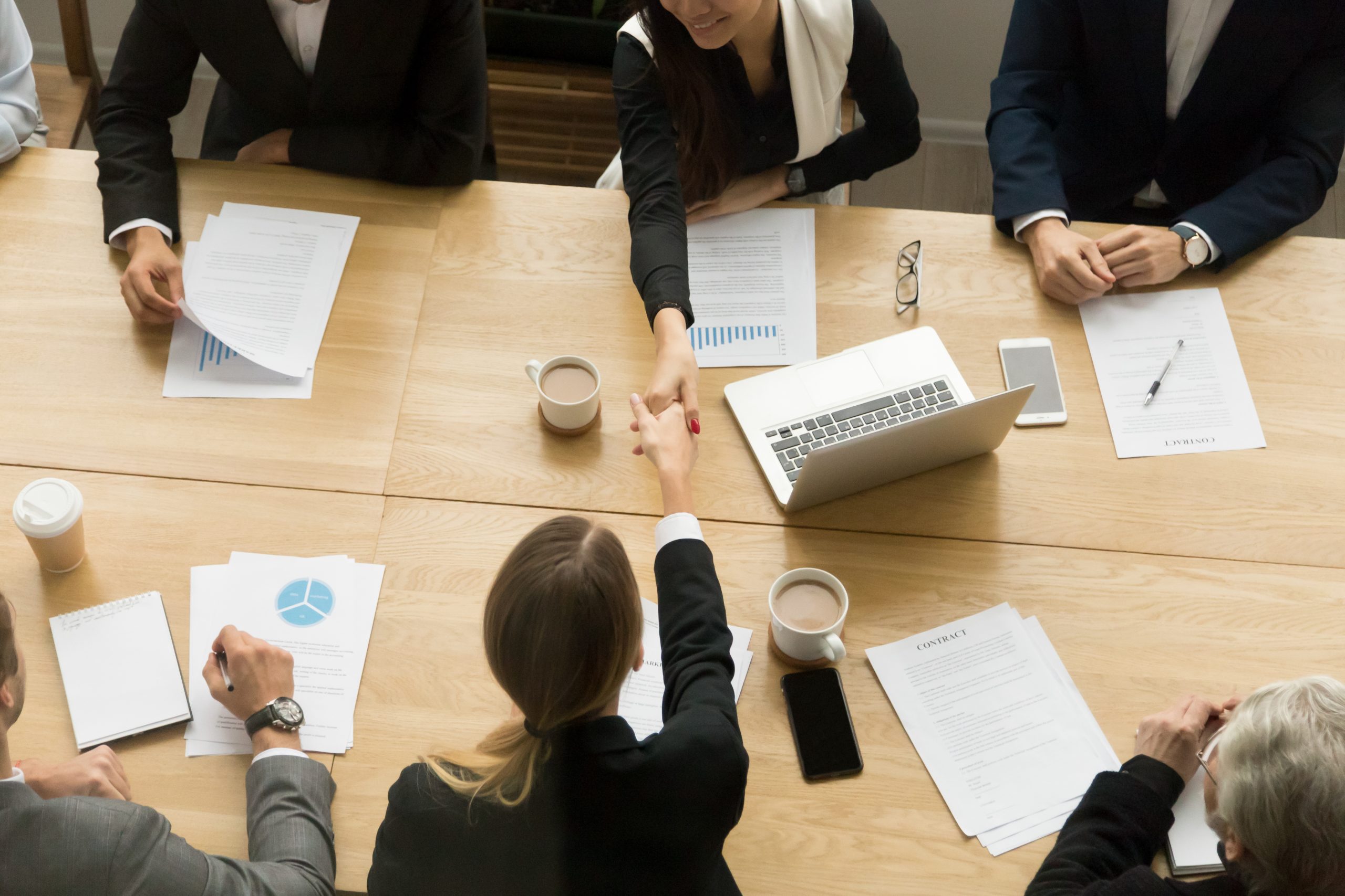 Two businesswomen shaking hands at group meeting, top view