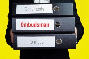 Ombudsman – finance/economics. Man carries a stack of 3 file folders. A folder has the label Ombudsman. Business, statistics concept