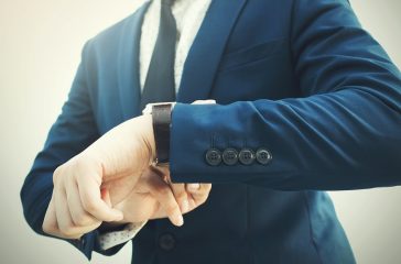 Fashionable businessman in elegant blue suit looking at luxury watch in hurry