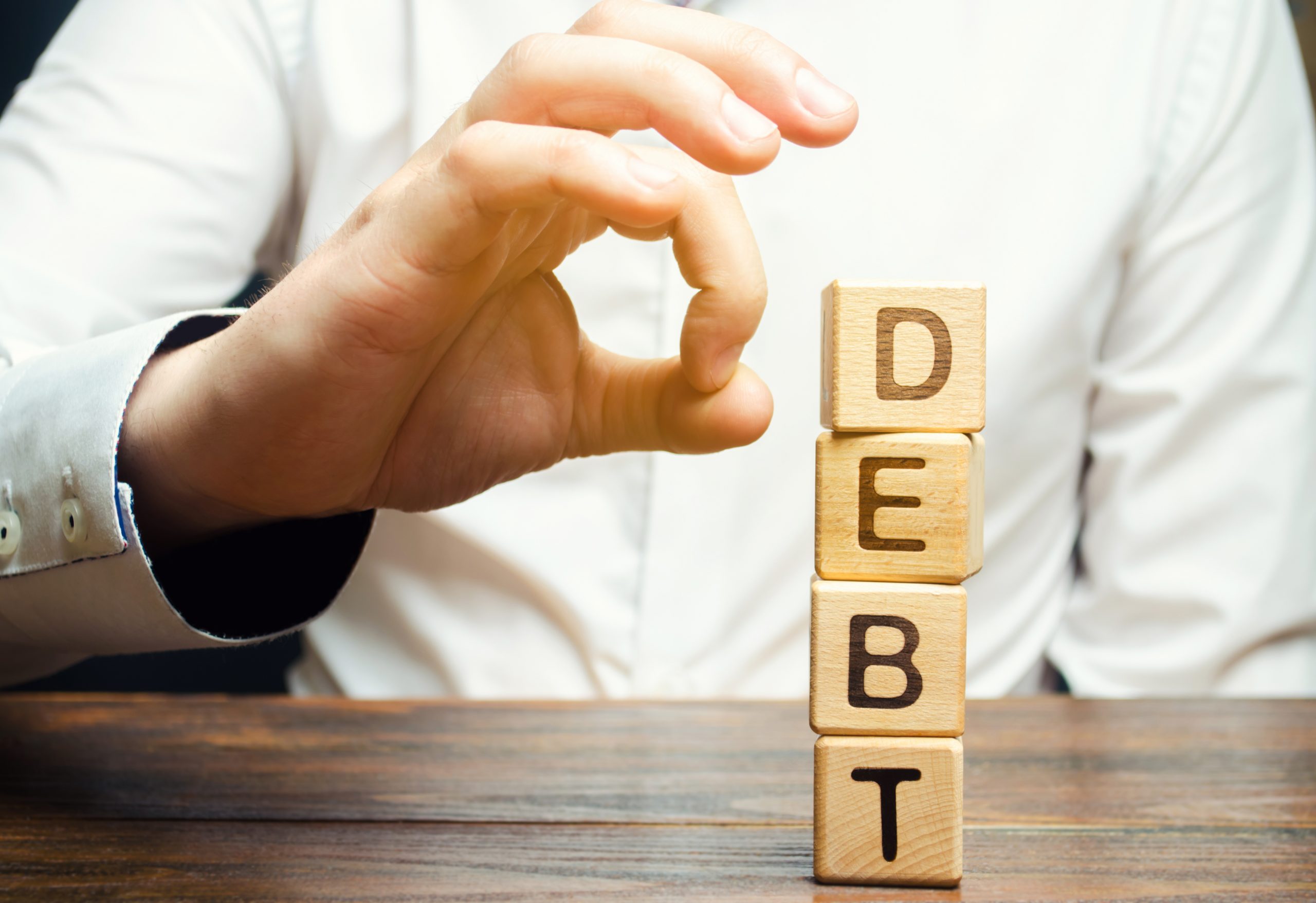 Businessman removes wooden blocks with the word Debt. Reduction or restructuring of debt. Bankruptcy announcement. Refusal to pay debts or loans and invalidate them. Debts service relief