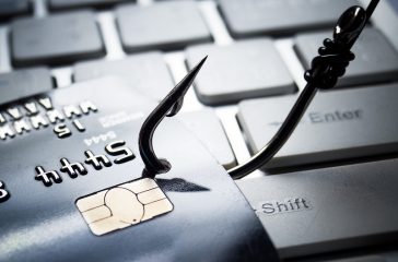 credit card phishing - piles of credit cards with a fish hook on computer keyboard