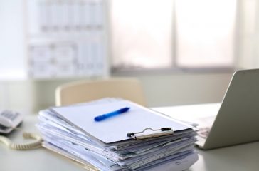 a stack of papers on the desk with a computer