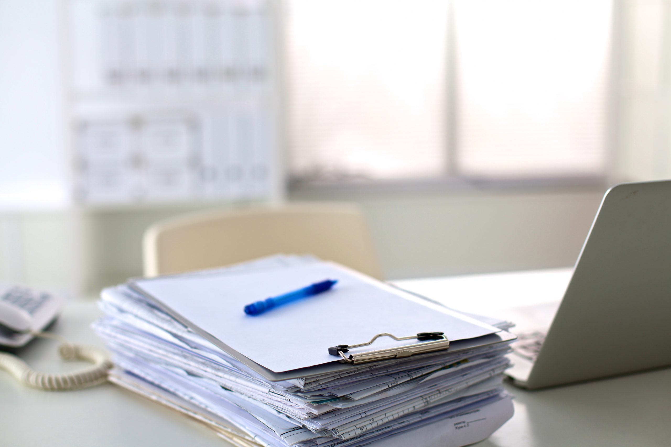 a stack of papers on the desk with a computer