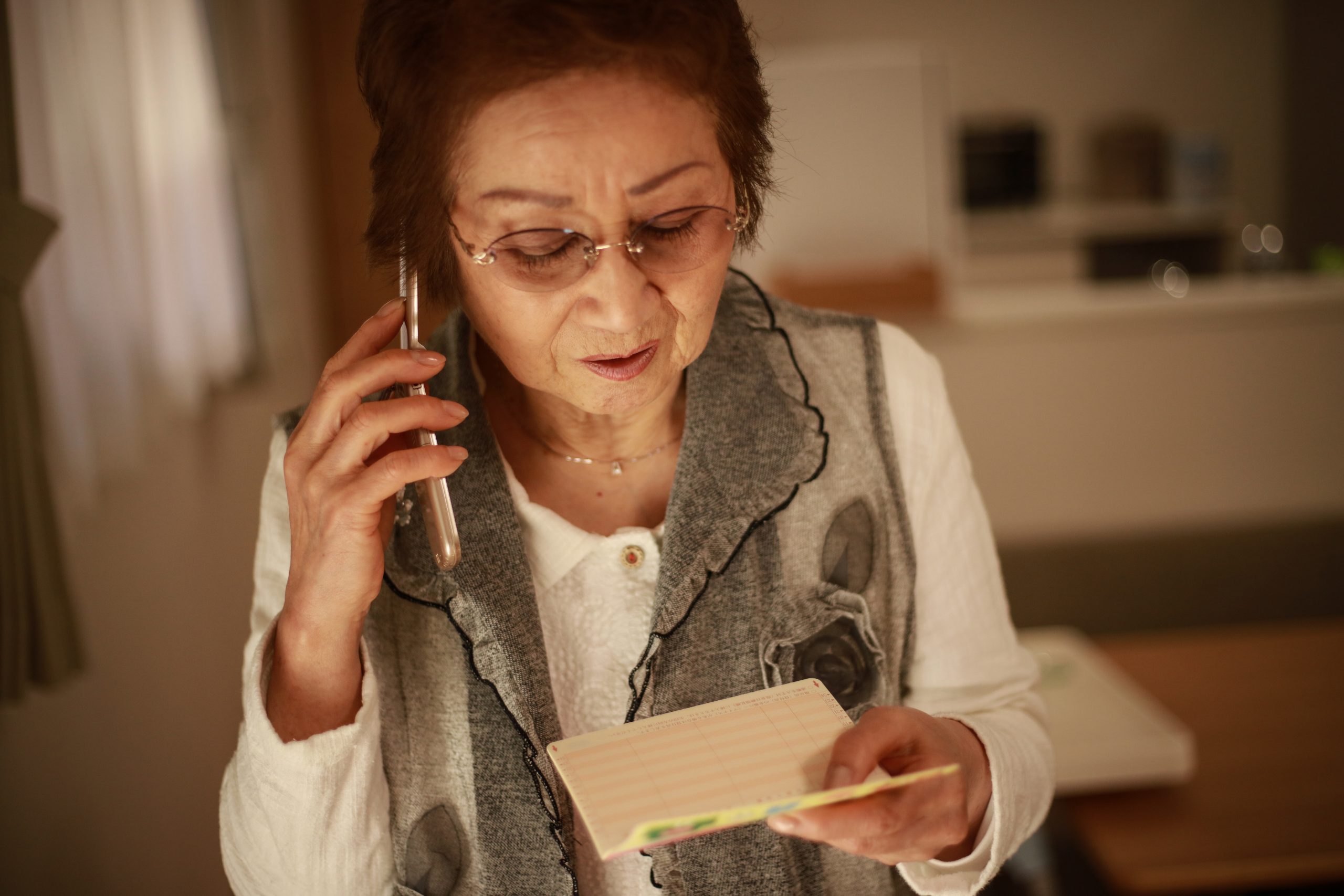 通帳を持ち通話するシニア女性