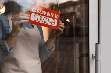 Woman in mask putting red sign with words "Closed Due To Covid-1