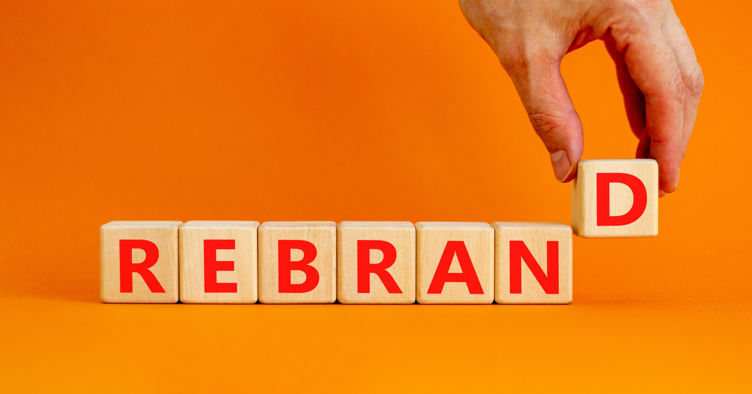 Rebrand and brand symbol. The concept word Rebrand on wooden cubes. Beautiful orange table, orange background, copy space. Businessman hand. Business rebrand and brand concept.