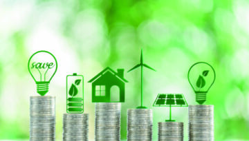 Renewable or clean energy generation prices and costs, financial concept : Green eco-friendly symbols atop coin stacks e.g. energy efficient light bulb, a battery, a solar cell panel, a wind turbine.